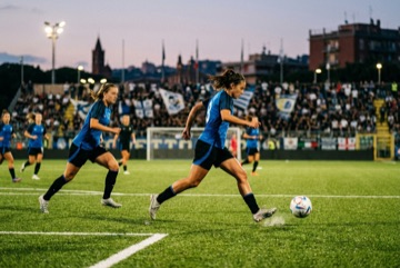 Calciatrici in divisa blu e nera durante una partita di calcio, con la palla in gioco
